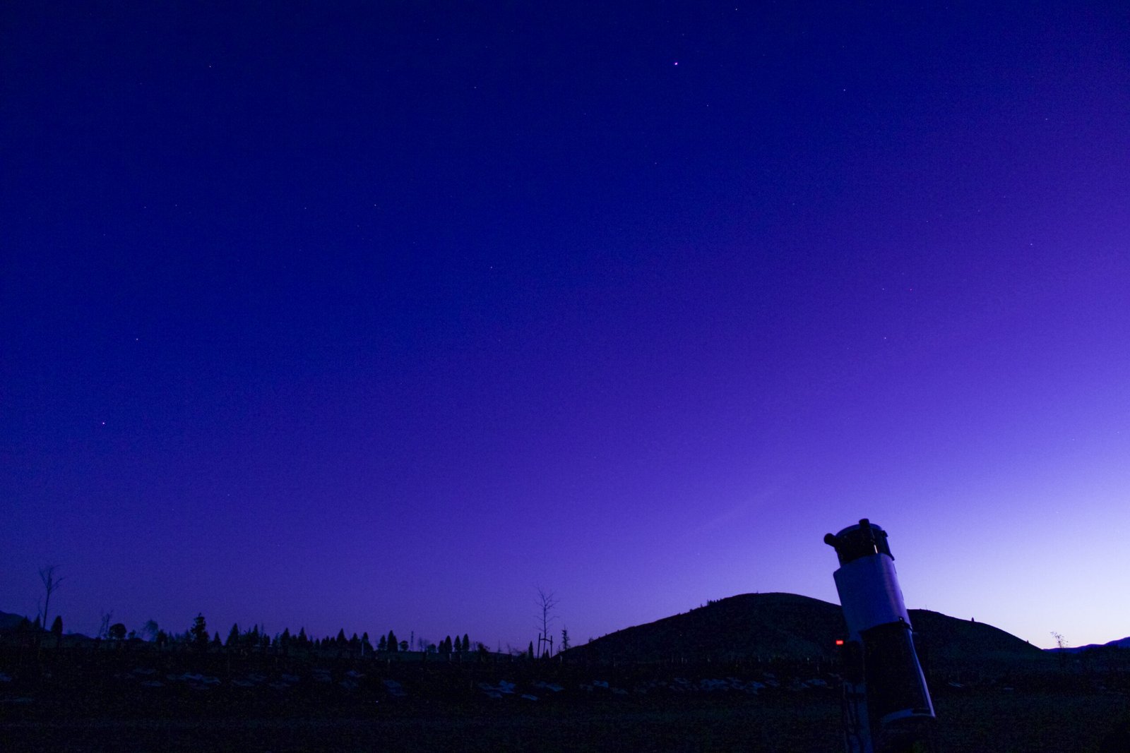 Telescope set up at dusk in Twizel with a colourful sunset and mountain silhouette in the background