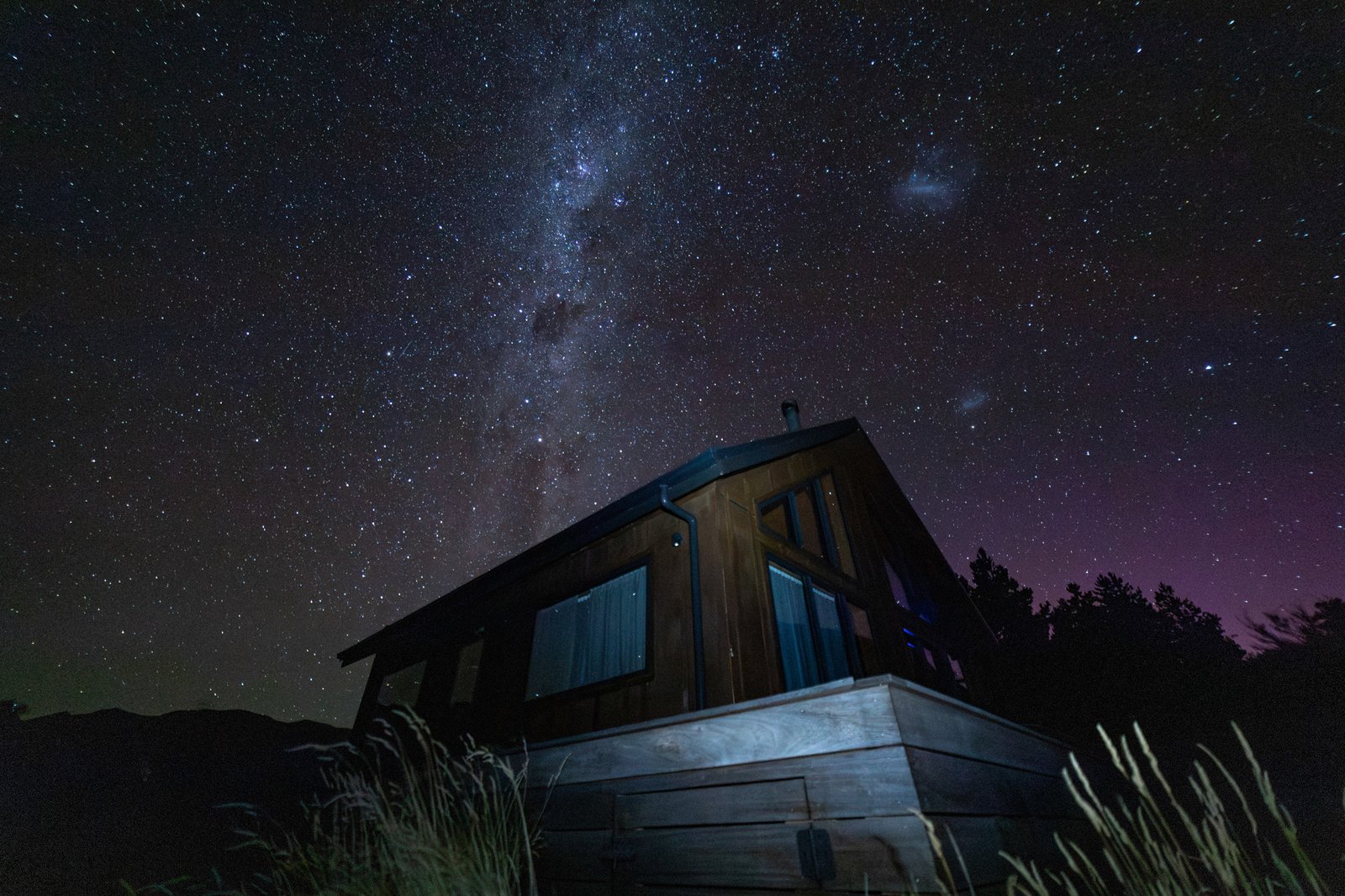 Cabin in the Southern Alps under a star-filled sky with the aurora in the background